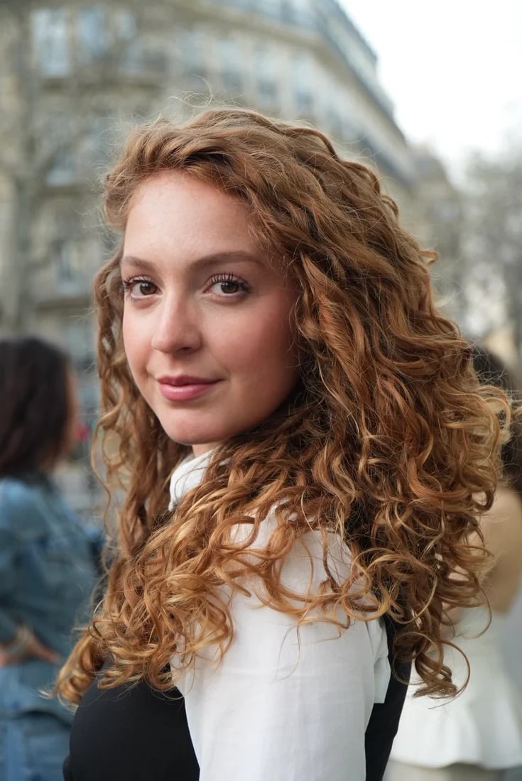 Flo, cheveux roux bouclés, regarde l’objectif par-dessus l’épaule dans une rue de Paris.
